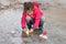 Cute little girl in rain boots playing with ships in the spring water puddle