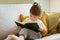 Cute little girl reading book while sitting on couch at home