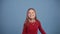 A cute little girl in a red sweater jumps and has fun on a blue background, waving her arms in different directions
