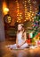 Cute little girl sits on the floor in the evening in the room near the festive Christmas tree