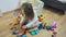 Cute little girl sits on floor and playing with colorful building blocks.