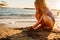 a cute little girl sits on the seashore, playing in the sand and with pebbles.