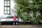 Cute little girl sitting on a bench by giant blossoming rose bush by a house in a typical Amsterdam street, Netherlands