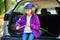 Cute little girl sitting in a car and using a pocket knife to whittle a hiking stick