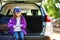 Cute little girl sitting in a car and using a pocket knife to whittle a hiking stick