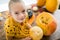 Cute little girl sitting on kitchen table, helping to carve large pumpkin, looking at camera and smiling. Halloween.