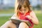 Cute little girl is sitting with a tablet on the grass in the park. Emotional portrait.