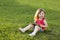 Cute little girl is sitting with a tablet on the grass in the park. Emotional portrait. Early education.