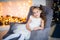 Cute little girl in smart white dress Christmas around the fireplace which decorated with holiday garland