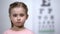 Cute little girl standing on background of visual acuity testing table, optics
