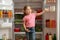 Cute little girl standing near open refrigerator