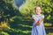 Cute little girl stands over blurred autumn garden background, extending big red apple in her palms to the camera