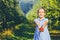 Cute little girl stands over blurred autumn garden background, extending big red apple in her palms to the camera