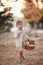 Cute little girl with a straw basket alone walks outdoors in a beautiful autumn park on a sunny day