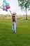 Cute little girl in straw hat holding colorful balloons in park
