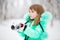 Cute little girl stretches her hand to catch falling snowflakes.