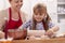 Cute little girl stretching the cookie dough - her mother supervising the operation