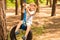 Cute little girl swinging on wheel attached to big tree in forest.