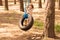 Cute little girl swinging on wheel attached to big tree in forest.