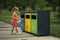Cute little girl throw plastic garbage into yellow container in a park