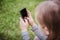 Cute little girl is using the smart phone. grass on background.