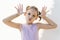 Cute little girl in violet dress make faces against white concrete wall. Joy, childhood