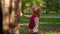 Cute little girl walks in the autumn forest with a tree. Child with curly blond hair in a pink vest on background of the