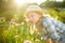 Cute little girl wearing straw hat admiring tall purple garlic flowers on sunny summer day. Child and flowers, summer, nature and