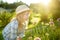 Cute little girl wearing straw hat admiring tall purple garlic flowers on sunny summer day. Child and flowers, summer, nature and