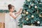 Cute little girl in a white dress decorating a Christmas tree on