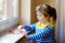 Cute little girl by window with lots of dough hearts as gift for Valentine& x27;s day, Mother& x27;s day or birthday. Adorable