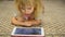 Cute Little Girl Works on Tablet Computer Lying on Carpet