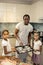 Cute little girls joining their father while putting cookies in to oven