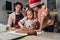 Cute little girls in red Santa hats with mother making homemade dough Christmas gingerbread cookies using cookie cutters together