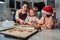 Cute little girls in red Santa hats with mother making homemade dough Christmas gingerbread cookies using cookie cutters together