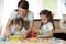 Cute little girls and their beautiful mom in aprons are playing and laughing while kneading the dough in the kitchen