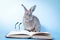 A cute little gray rabbit is reading a book and has a small pair of glasses nearby.