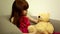 Cute little happy girl calm child kid sitting in chair talks looking lovingly at her big stuffed plush bear toy playing