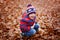 Cute little kid boy on autumn leaves background in park.