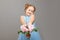 A cute little kid girl in a blue dress holds in her hands a bouquet of flowers. Gray background, portrait, studio