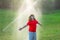 Cute little kid watering grass in the garden at summer day. Child play in summer backyard. Cute little boy is laughing