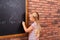 Cute little left-handed girl drawing on chalkboard near wall