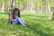Cute little long-haired girl sitting on the grass in a park with a mobile phone in her hands and sending message on phone mobile