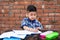 Cute little male student in school uniform writing on notebook while attending class in Primary school. He is using pencil for