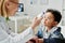 Cute little multiethnic boy looking at thermometer held by mature doctor