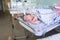Cute little newborn baby sleeping in infant bed in hospital, folded hands with open mouth