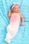 Cute little newborn girl lying on blue furry blanket wearing pas