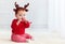 Cute little redhead baby boy with reindeer band tasting christmas sweet treats, sitting on the floor at home