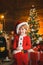 Cute little santa baby with New years gifts on Christmassy background. Christmas attributes. Childhood memories. Family