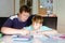 Cute little school kid boy at home making homework with dad. Little child writing with colorful pencils, father helping